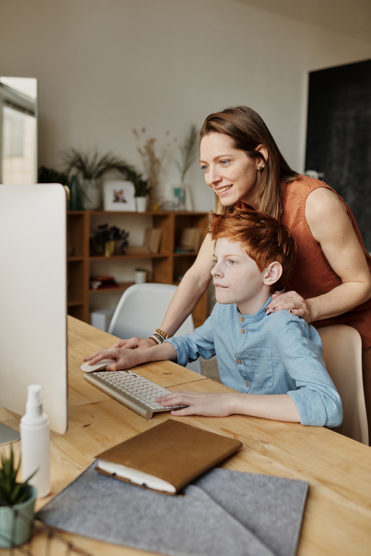 A woman and boy sitting at a table with a computer.