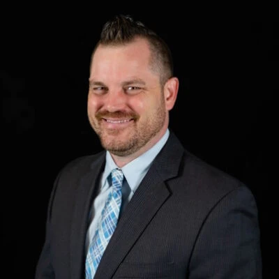 Mike Repenning, an engineer, smiling at the camera in a black suit and blue striped tie.