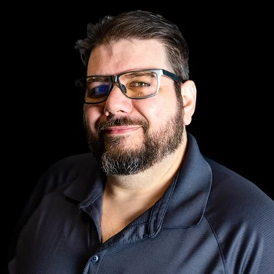 The CISO of Certified CIO, Shaun, in a black shirt and wearing glasses while smiling at the camera.