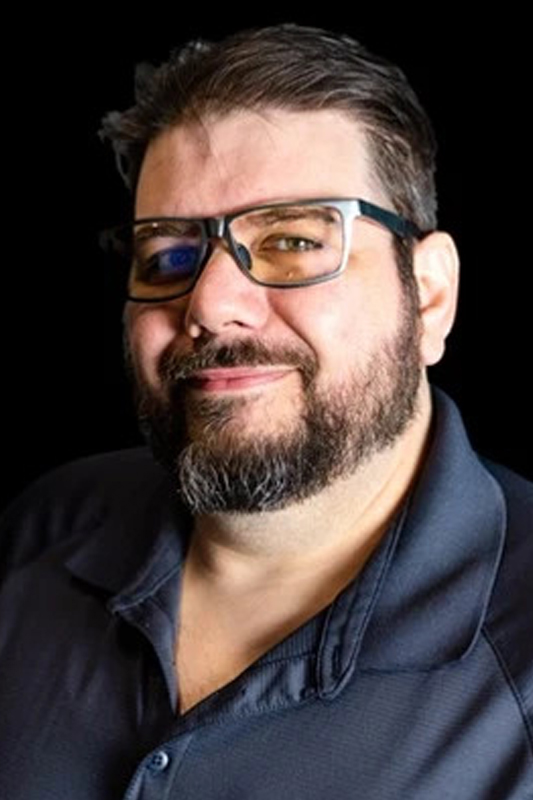 The CISO of Certified CIO, Shaun, in a black shirt and wearing glasses while smiling at the camera.